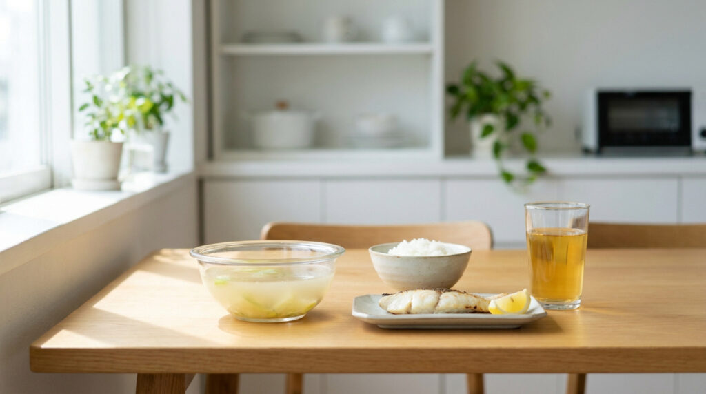 Un bol de soupe, un bol de riz blanc et un filet de poisson cuit avec un quartier de citron sur une table en bois.