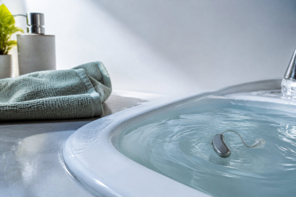 Un appareil auditif repose au fond d'un lavabo rempli d'eau, avec une serviette et un distributeur de savon à proximité.