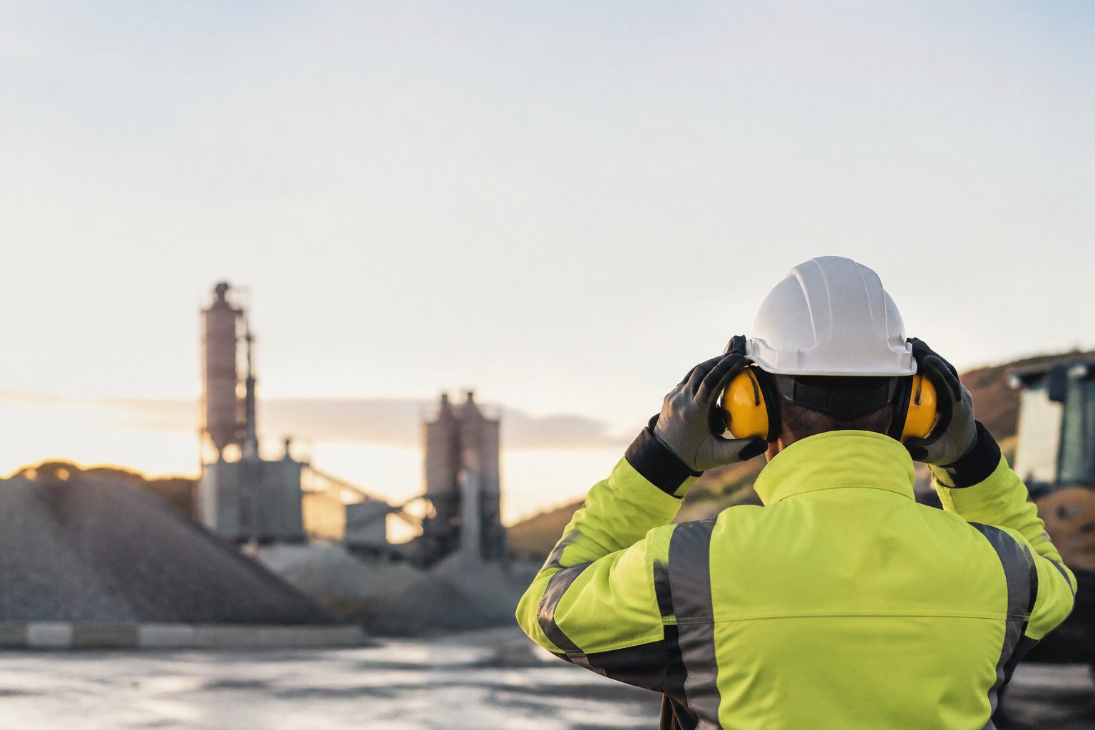 Ouvrier en équipement de protection individuelle ajustant son casque antibruit face à une carrière industrielle.