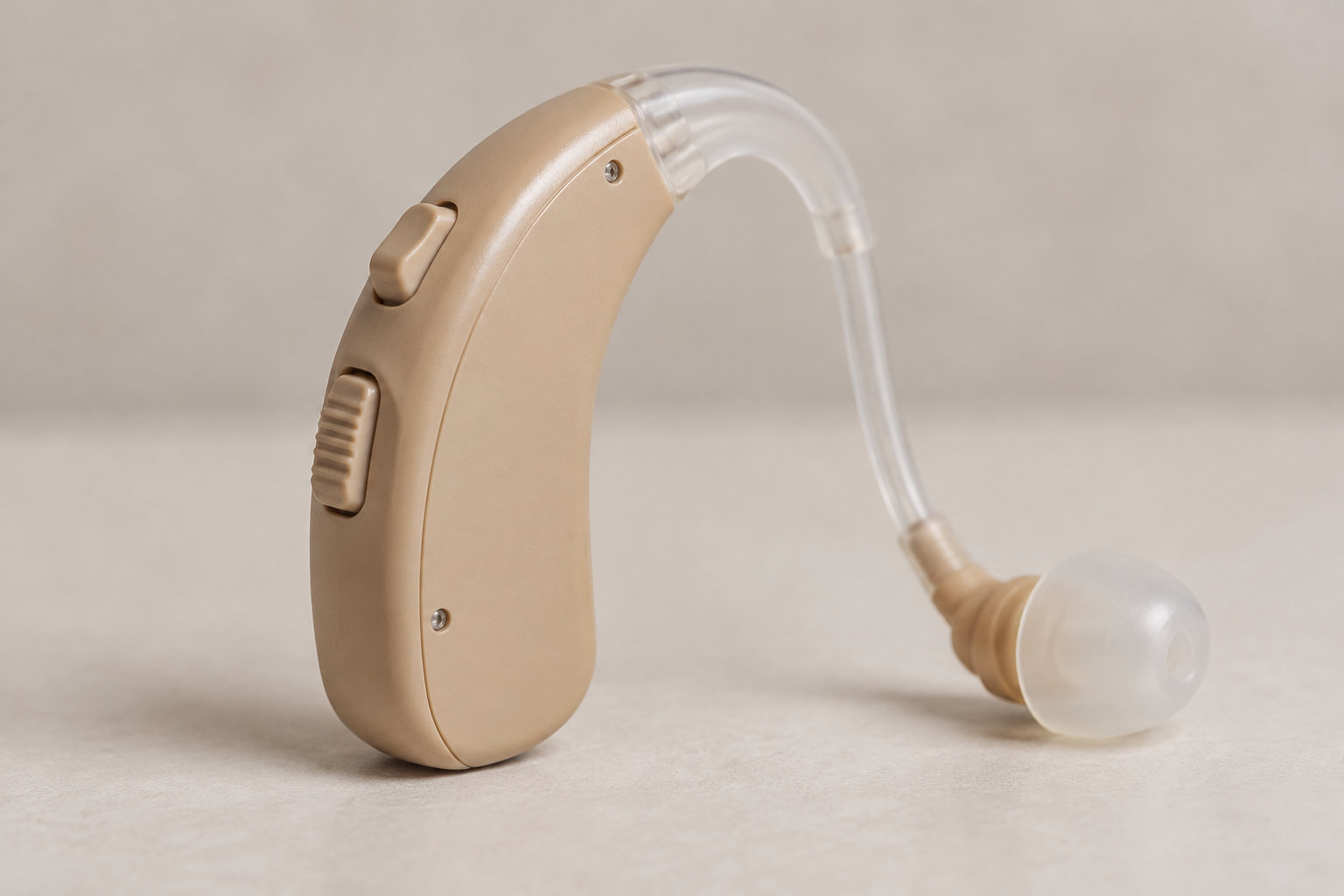 Un appareil auditif beige avec un tube transparent et un embout repose sur une surface claire.